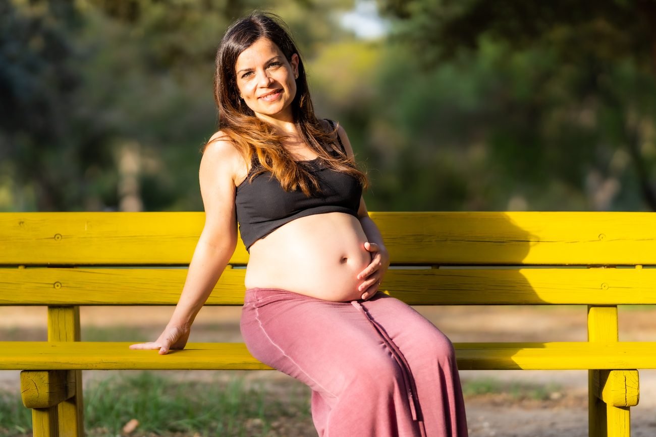 Pregnant woman sitting on a yellow park bench