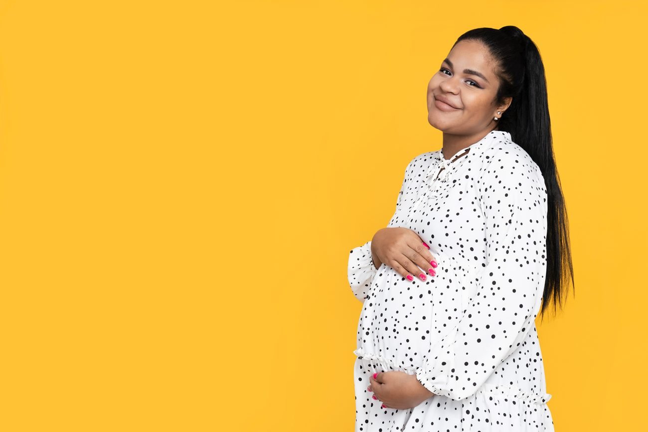 Pregnant woman in white dress on yellow background